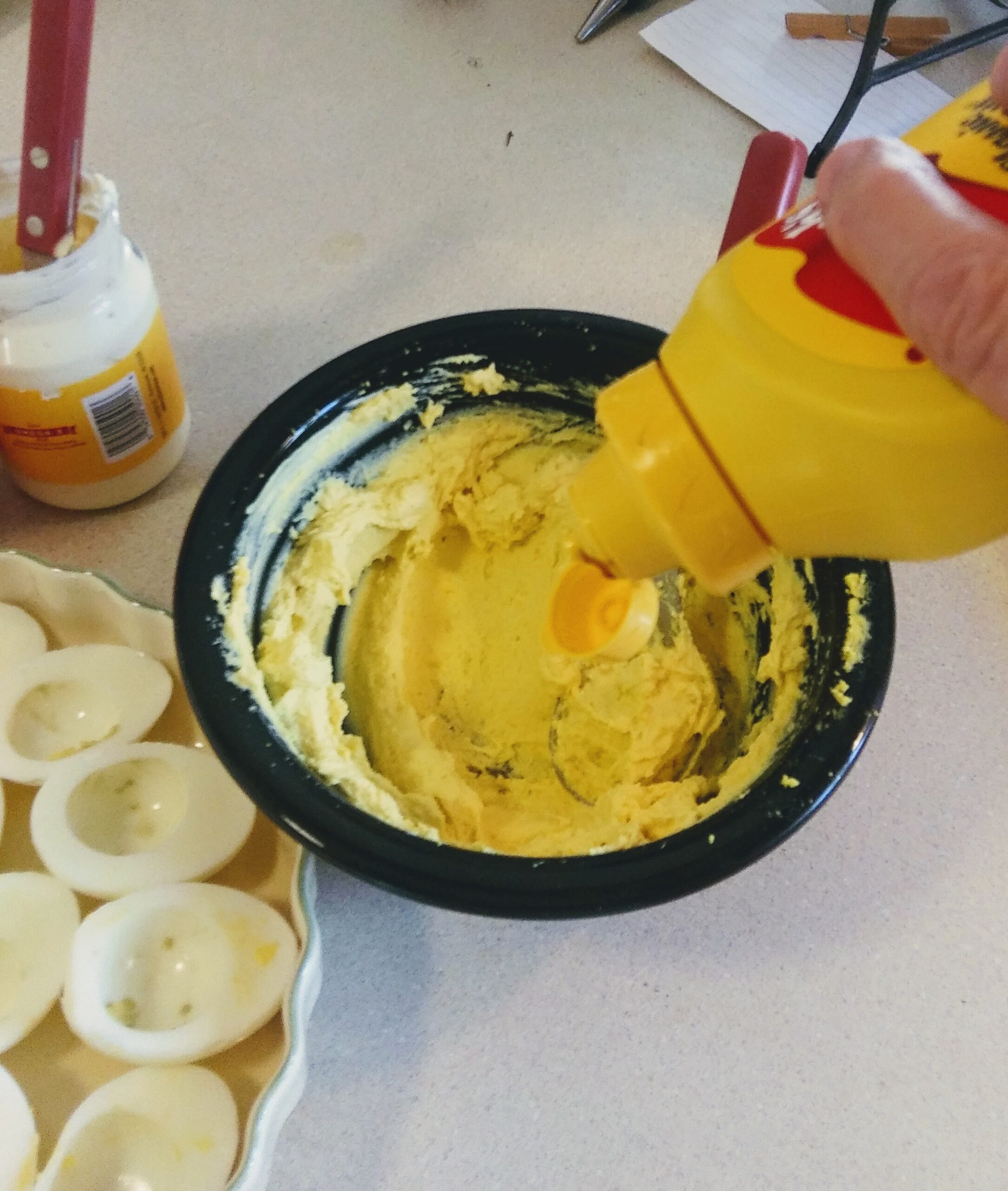 Adding mustard, mayonnaise, and sour cream to cooked yolks.